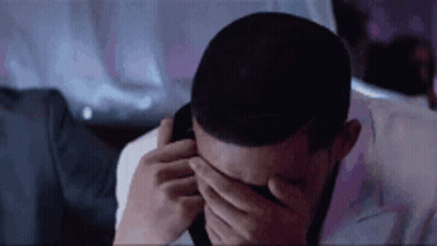 A Man Is Covering His Eyes With His Hands While Talking On A Cell Phone . GIF