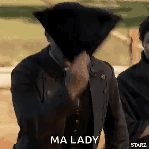 A Man Is Covering His Face With A Hat While Standing Next To Another Man . GIF