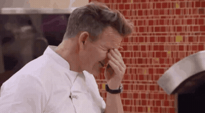 A Man Is Covering His Face With His Hands In Front Of A Red Tiled Wall . GIF