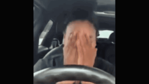 A Man Is Covering His Face With His Hands While Driving A Car . GIF