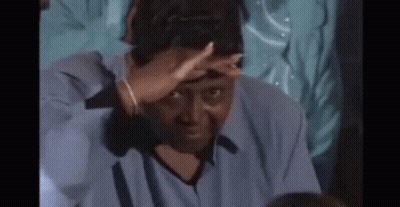 A Man Is Covering His Face With His Hands While Sitting In A Dark Room . GIF