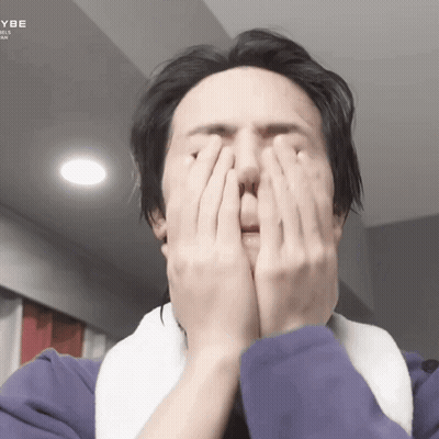 A Man Is Covering His Face With His Hands While Wearing A Purple Jacket GIF