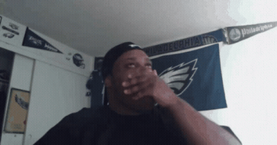 A Man Is Covering His Mouth In Front Of A Philadelphia Flag GIF