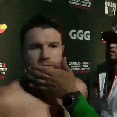 A Man Is Covering His Mouth In Front Of A Sign That Says Ggg GIF