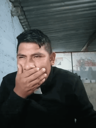 A Man Is Covering His Mouth With His Hand In Front Of A Sign That Says Trabajo Educacion GIF