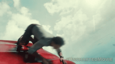 A Man Is Crawling On The Roof Of A Red Car With #Unchartedmovie Written Below Him GIF