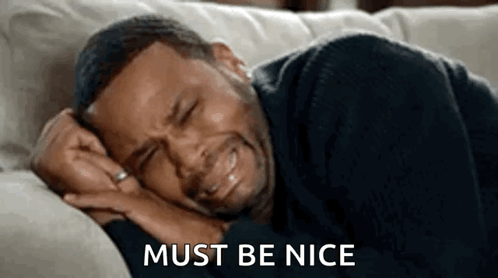 A Man Is Crying While Laying On A Couch And The Words `` Must Be Nice '' Are Next To Him . GIF