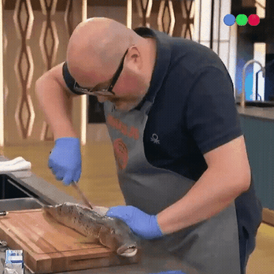 a man is cutting a fish on a cutting board while wearing a shirt that says benetton