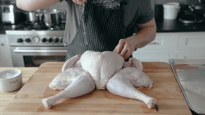 A Man Is Cutting A Turkey On A Wooden Cutting Board GIF