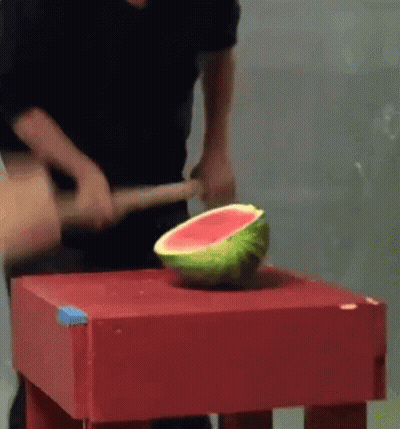 A Man Is Cutting A Watermelon With A Hammer On A Table . GIF