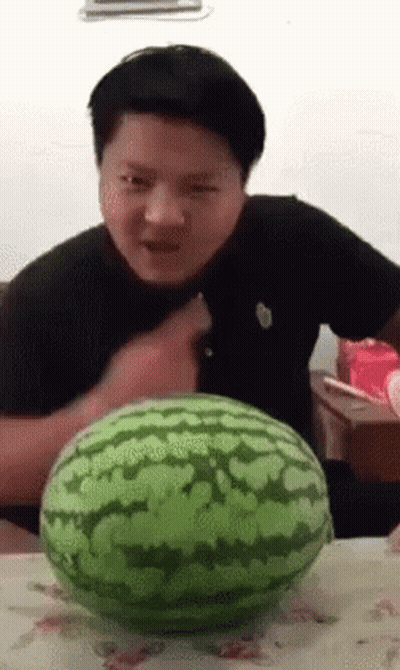 A Man Is Cutting A Watermelon With A Knife While Sitting At A Table . GIF
