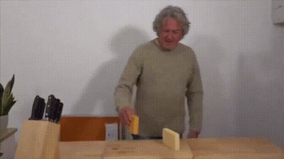 A Man Is Cutting Cheese On A Cutting Board GIF