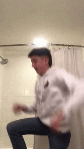 A Man Is Dancing In A Bathroom With A Shower Curtain Behind Him . GIF