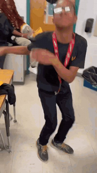 A Man Is Dancing In A Classroom While Wearing Glasses And A Lanyard . GIF