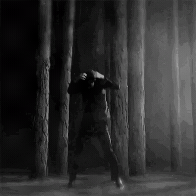 A Man Is Dancing In A Dark Forest Surrounded By Trees . GIF