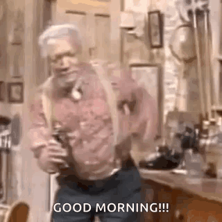 A Man Is Dancing In A Kitchen With A Bottle Of Beer In His Hand . GIF