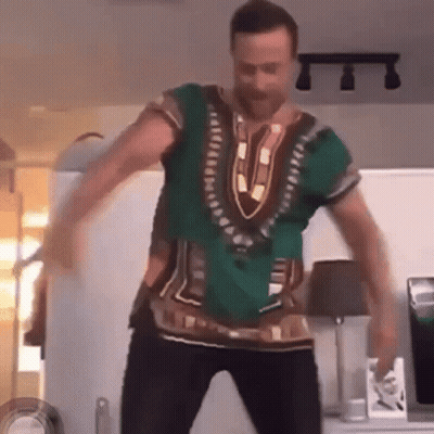 A Man Is Dancing In A Living Room Wearing A Green Shirt . GIF