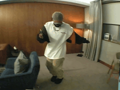 A Man Is Dancing In A Living Room Wearing A Hat And A White Shirt GIF