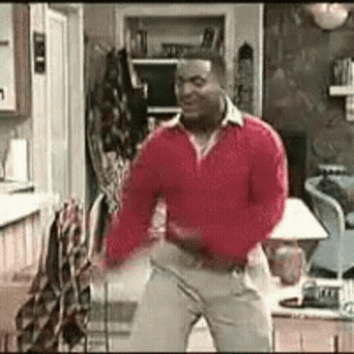 A Man Is Dancing In A Living Room Wearing A Red Sweater And Khaki Pants . GIF