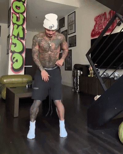 A Man Is Dancing In A Living Room With A Graffiti Wall That Says ' Dunzo ' On It GIF