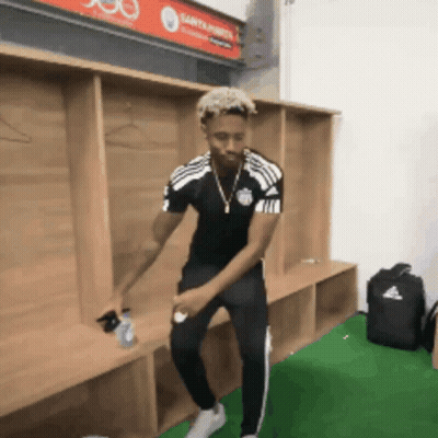 A Man Is Dancing In A Locker Room With A Sign That Says Santander On It GIF
