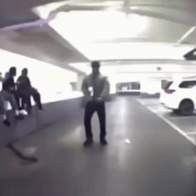 A Man Is Dancing In A Parking Garage While A Group Of People Sit On A Bench . GIF