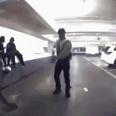 A Man Is Dancing In A Parking Garage With People Sitting On Benches . GIF