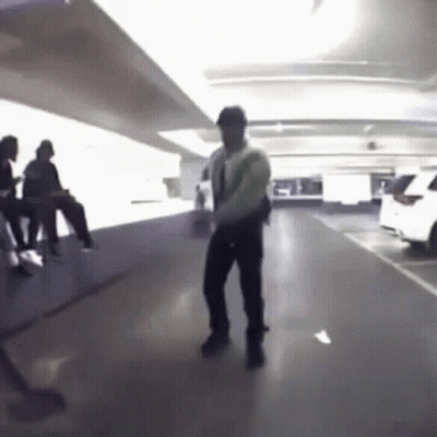 A Man Is Dancing In A Parking Garage With People Sitting On The Floor . GIF