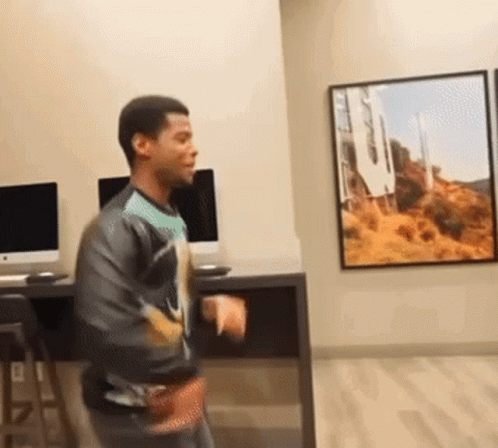 A Man Is Dancing In A Room With A Picture Of Hollywood On The Wall . GIF