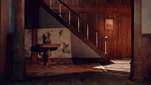 A Man Is Dancing In A Room With Stairs Behind Him GIF