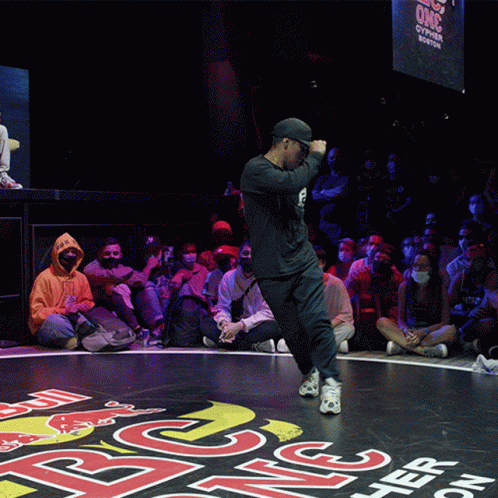 A Man Is Dancing In Front Of A Crowd That Is Sitting On The Floor Watching GIF