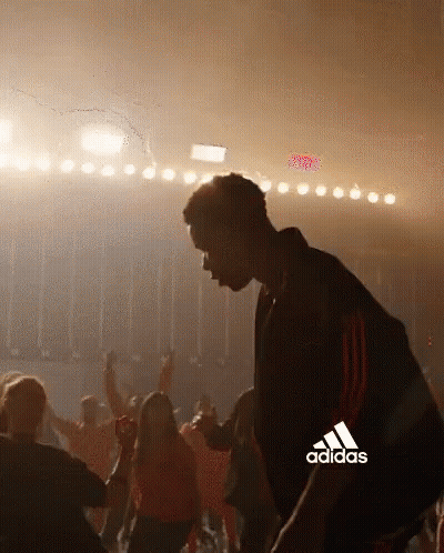 A Man Is Dancing In Front Of A Crowd With The Adidas Logo In The Background . GIF
