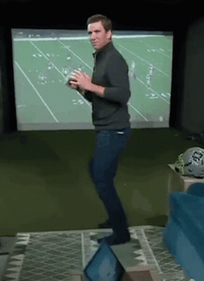A Man Is Dancing In Front Of A Football Screen While Holding A Football . GIF