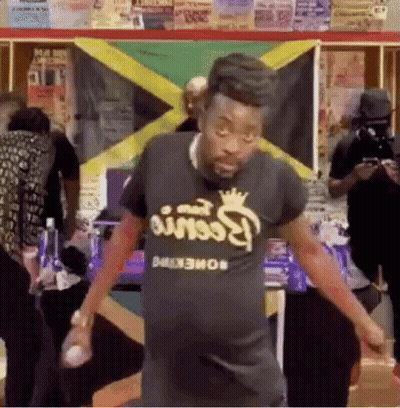 A Man Is Dancing In Front Of A Jamaican Flag In A Room . GIF