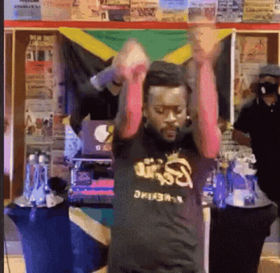 A Man Is Dancing In Front Of A Jamaican Flag While Wearing A Black Shirt . GIF