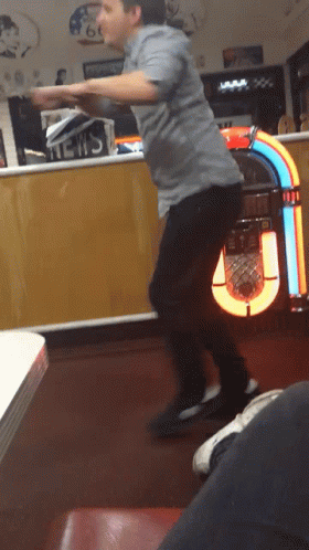 A Man Is Dancing In Front Of A Jukebox That Has The Word News On It GIF