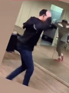 A Man Is Dancing In Front Of A Mirror With A Suitcase GIF