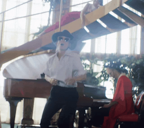 A Man Is Dancing In Front Of A Piano While A Woman Plays A Piano GIF