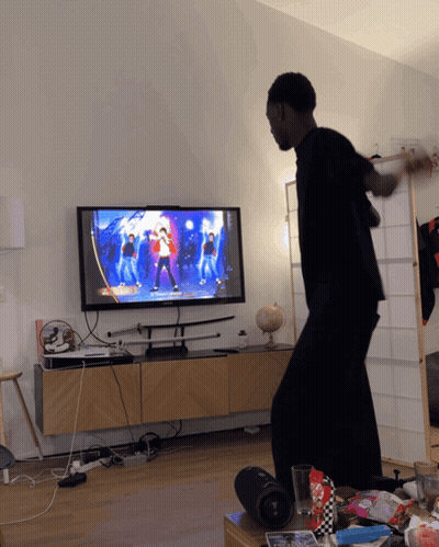 A Man Is Dancing In Front Of A Tv That Shows A Dance Video GIF
