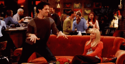 A Man Is Dancing In Front Of A Woman Sitting On A Red Couch GIF