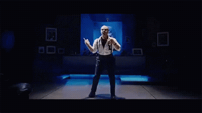 A Man Is Dancing On A Stage In A Dark Room . GIF