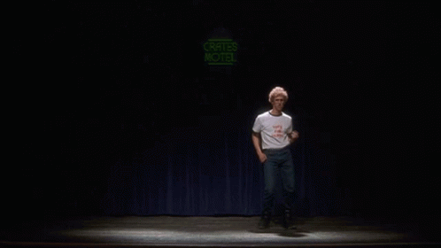 A Man Is Dancing On A Stage In Front Of A Neon Sign That Says Crates Motel GIF
