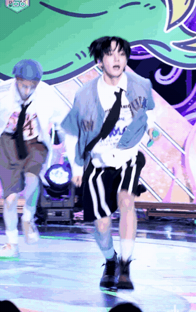 A Man Is Dancing On A Stage While Holding A Microphone And Wearing A Tie . GIF