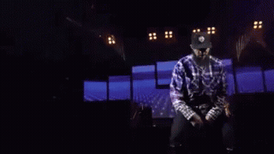 A Man Is Dancing On A Stage With A Knife In His Hand In A Dark Room . GIF