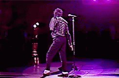 A Man Is Dancing On A Stage With A Microphone In Front Of Him GIF
