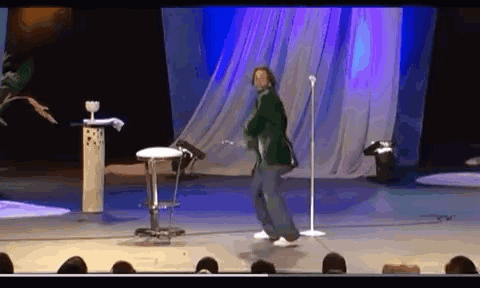 A Man Is Dancing On Stage In Front Of A Microphone . GIF