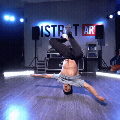 A Man Is Doing A Handstand In Front Of A Wall That Says District Art GIF