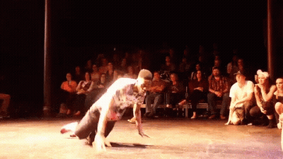 A Man Is Doing A Handstand On A Stage In Front Of A Crowd GIF