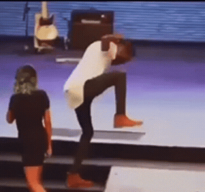 A Man Is Doing A Handstand On A Stage While A Woman Watches . GIF