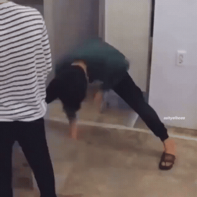 A Man Is Doing A Handstand On The Floor In Front Of A Mirror While Another Man Stands Behind Him . GIF
